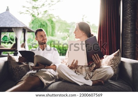 Caucasian couple in love discussing journal article during weekend spending at comfortable couch at house terrace, intelligent husband and wife talking about magazine reading and hobby preference