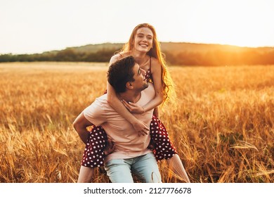 Caucasian Couple Man Giving Woman Piggy Back Ride Through The Wheat Field, Together At Sunset. Activity Relationship.