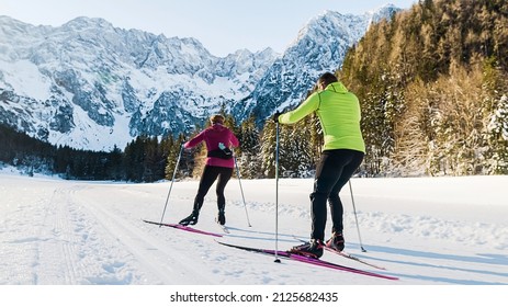 Caucasian Couple Moving In Sync While Cross Country Skiing On The Ski Trail Surrounded By Mountains And Forest.