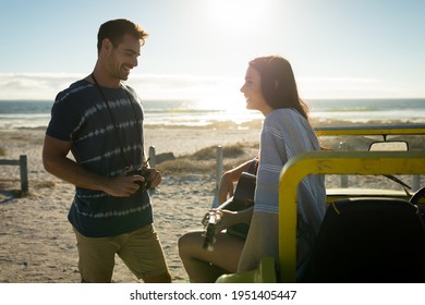 Caucasian couple on beach, man holding camera smiling, woman sitting on beach buggy playing guitar. beach break on summer holiday road trip. - Powered by Shutterstock