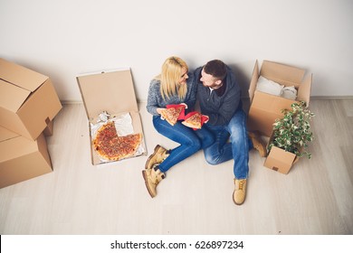 Caucasian Couple Taking A Break, Eating Pizza And Sitting On The Floor In New Apartment