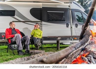 Caucasian Couple In Their 40s Drinking Wine In Front Of Their Modern RV Camper Van. Campsite Family Fun. Rving Theme.