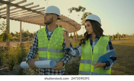 Caucasian coworkers architect partnership male man businessman engineer hold blueprint explaining talk female businesswoman inspector woman writing clipboard report pointing finger project scheme park - Powered by Shutterstock