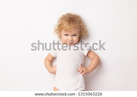 Caucasian curly baby girl in a white T-shirt on a white background hands holding a waist. child hands in hips.