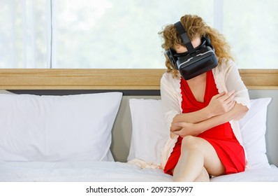 Caucasian Curly Long Hair Pregnancy Female Mother In Red Maternity Dress Pajama With Rope Wears Vr Goggles Sitting Smiling Lay Down On Bed Learning Study Practice Virtual Reality Babysitting Online.