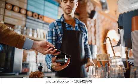 Caucasian Customer Pays for Coffee and Pastry with Contactless NFC Payment Technology on Smartphone to a Handsome Barista in Blue Checkered Shirt. Contactless Mobile Payment in Cafe Concept.