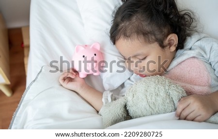Caucasian Cute female child sleeping on a piggybank on bedroom.Baby taking a nap and a piggy bank.Childcare cost life insurance.