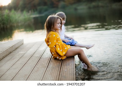 Caucasian cute girl and boy together on the footpath by the lake, happy childhood in the village, children play in the park near the water, children dangle their feet in the water of the lake - Powered by Shutterstock