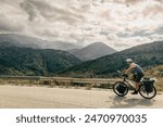 Caucasian cyclist solo bicycle touring around mountains in summer with scenic mountain rage background outdoors.