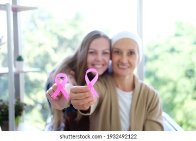 Caucasian daughter and Elderly mother in white headscarf is holding Awareness pink ribbon of common cancer is symbol of various campaign activities for patients with breast cancer. Focus on women hand - Shutterstock ID 1932492122