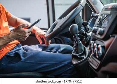 Caucasian Delivery Truck Driver Browsing Internet Using His Smartphone. Van Vehicle Interior. - Powered by Shutterstock