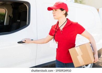 Caucasian Delivery Woman Carrying A Small Box After Picking Up Some Packages To Deliver At A Shipping Address. Female Courier Opening The Door Of A Delivery Van