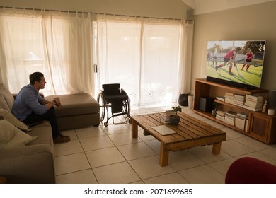 Caucasian Disabled Man Sitting At Home Watching Cricket Match On Tv. Sports, Competition, Entertainment And Technology Concept Digital Composite Image.