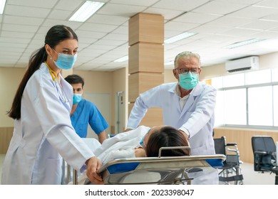 Caucasian doctor and Asian male nurse moving injured patient from an accident on a gurney to the emergency operating room. Medical team pushing an patient on the bed into urgent surgery at a hospital