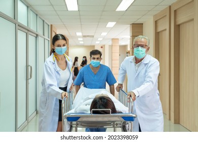 Caucasian doctor and Asian male nurse moving injured patient from an accident on a gurney to the emergency operating room. Medical team pushing an patient on the bed into urgent surgery at a hospital - Powered by Shutterstock