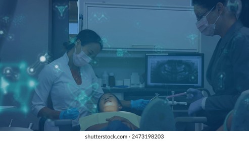 Caucasian doctor examining Asian child, with an Asian nurse assisting. They are in dental clinic, using advanced technology displayed on screens - Powered by Shutterstock