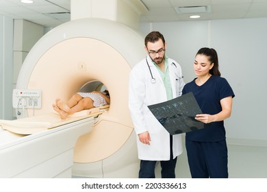 Caucasian Doctor And Radiologist Technician Checking The MRI Spine Resonance Of A Female Patient In The Medical Imaging Lab