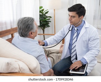 Caucasian Doctor Sit On Chair Check Asian Senior Elderly Old Man Heart Beat Lay Down On Sofa At Home.Medicine And Healthcare Concept.