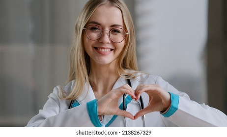 Caucasian Doctor Specialist Nurse Woman Practitioner Therapist In Glasses In Clinic Hospital At Table Shows Heart Shape Sign Of Mercy Love Kindness Assistance Medicine Help International Medical Day