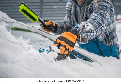 Caucasian Driver Removing Snow And Ice From His Car Windshield. Extreme Winter Season Weather And The Car Maintenance. Automotive Theme.