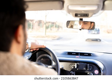 Caucasian or eastern man with hands holding driving wheel riding car on sunny autumn, winter or spring day. Travel, exam, lesson, learning, taxi driver. View from back seat, face in rearview mirror