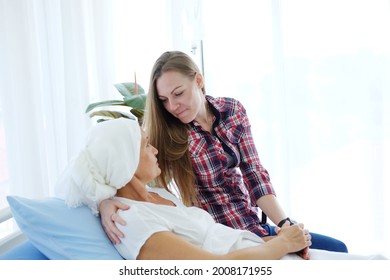 Caucasian Elderly Mother In White Headscarf Is Laying On Bed In Hospital After Chemotherapy Because She Is Suffering From Cancer Or Leukemia Patient And Young Daughter Is Hugging And Caring Her Mom.