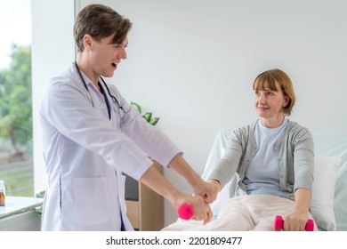 Caucasian Elderly Patient Woman Sitting On Bed And Lifting Dumbbell To Exercise After Treatment In Hospital. Workout Exercise With Doctor. Healthcare Medical And Physiotherapist Insurance Concept