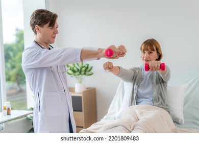 Caucasian Elderly Patient Woman Sitting On Bed And Lifting Dumbbell To Exercise After Treatment In Hospital. Workout Exercise With Doctor. Healthcare Medical And Physiotherapist Insurance Concept