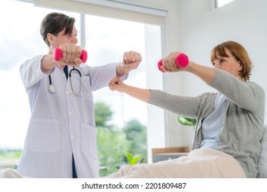 Caucasian Elderly Patient Woman Sitting On Bed And Lifting Dumbbell To Exercise After Treatment In Hospital. Workout Exercise With Doctor. Healthcare Medical And Physiotherapist Insurance Concept