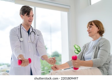 Caucasian Elderly Patient Woman Sitting On Bed And Lifting Dumbbell To Exercise After Treatment In Hospital. Workout Exercise With Doctor. Healthcare Medical And Physiotherapist Insurance Concept