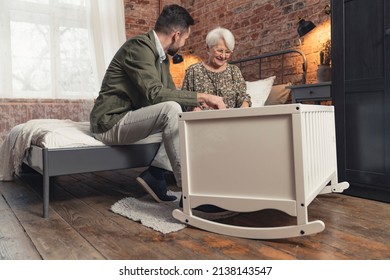 caucasian elegant novice dad and his elderly mother sitting next to the white cradle where grandchild is napping. High quality photo - Powered by Shutterstock