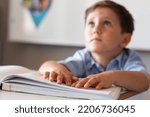 Caucasian elementary schoolboy sitting with hands on braille at desk in classroom. unaltered, education, childhood, studying, blindness, disability, learning and school concept.