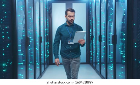 Caucasian IT Engineer Activating Digital Database Server Room With Tablet. Bearded Specialist Inspecting Rack Internet Servers At Data Center Computer Security. Zoom Out.