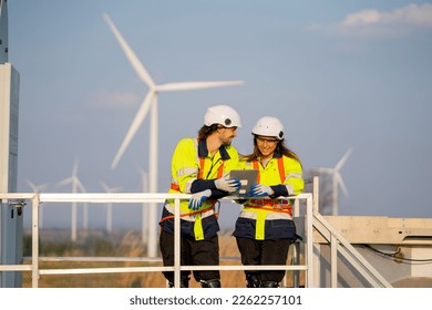 Caucasian engineer man and woman discuss with happiness together with woman hold tablet and they stay on base of windmill and in front of row of wind turbine with blue sky and warm evening light. - Powered by Shutterstock