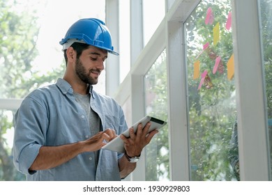 Kaukasischer Ingenieur arbeitet im Büro mit Glasfenstern und verwenden Tablette zu verwalten System auch Kontakt mit anderen Mitarbeiter.