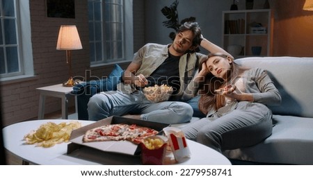 Caucasian extremely frustrated couple sitting in front of tv watching shows and eating pizza in absolute boredom. Student couple tired after a long day 