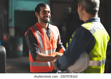 Caucasian factory engineer talking and shaking hands on business cooperation agreement. Successful hand shaking after good deal, workers handshaking each other at heavy industrial production line. - Powered by Shutterstock