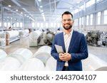 Caucasian factory manager or CEO holding tablet computer and checking production results in industrial plant while employees working in background.