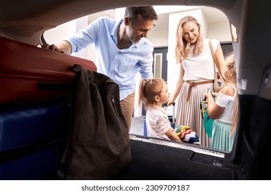 Caucasian family of four packing luggage into car trunk for holiday - Powered by Shutterstock