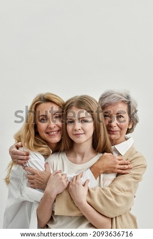 Caucasian family of grandmother, mother and granddaughter hugging and looking at camera. Age and generation concept. Family relationship and closeness. White background. Studio shoot. Copy space