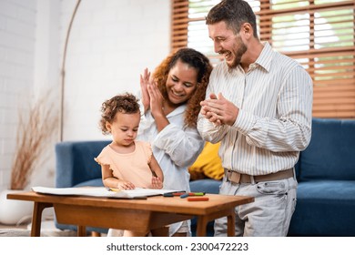 Caucasian family painting paper and daughter indoors in house  Happy family activity  Little baby girl children learn how to draw art picture enjoy creativity and mother   father in living room