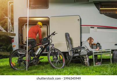 Caucasian Family RV Camping Time. Father And His Daughter In Front Of Their Rental RV Camper Van. Mountain Bike And Camping Furnitures. Men Looking Inside Cargo Area.