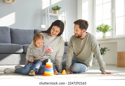 Caucasian family with their little daughter builds rainbow tower while playing on floor of children's room. Mom, dad and toddler girl have fun together. Concept of parenting and child development. - Powered by Shutterstock