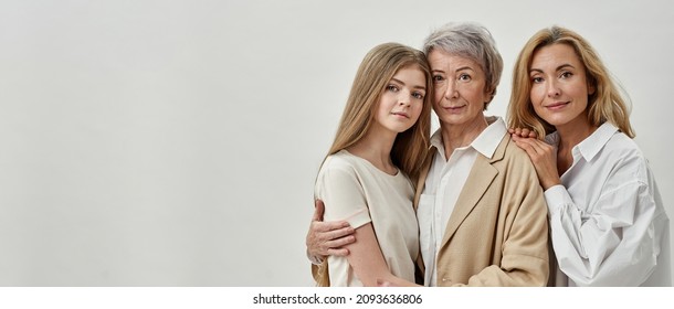 Caucasian family of three female generations hugging each other and looking at camera. Age and generation concept. Grandmother, mother and granddaughter. White background. Studio shoot. Copy space