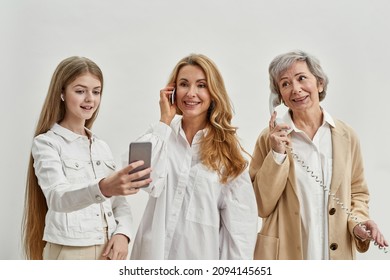 Caucasian Family Of Three Female Generations Use Variety Phones. Age And Generation Concept. Senior Woman Talk On Landline Phone. Adult Woman Talk On Cellphone. Teenage Girl Take Selfie On Smartphone