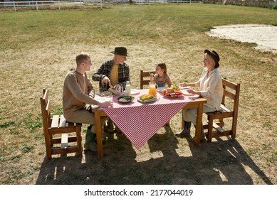 Caucasian Farming Family Having Lunch Or Dinner With Fresh Organic Products On Lawn In Countryside Outdoors. Grandparents And Grandchildren Spending Time Together. Modern Farm Lifestyle. Sunny Day