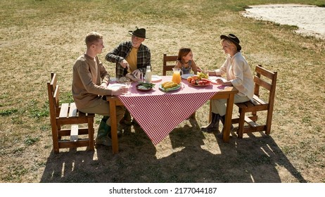 Caucasian Farming Family Having Lunch With Fresh Organic Products On Lawn In Countryside Outdoors. Grandparents And Grandchildren Enjoying Time Together. Modern Farm Lifestyle. Sunny Day