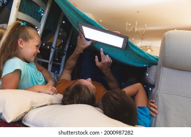 Caucasian Father With Daughter And Son Smiling, Lying In Blanket Fort Using Tablet At Home. Childhood With Technology, Spending Free Time At Home.