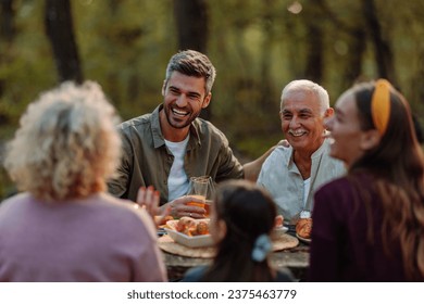 Caucasian father and his father, the grandfather, are laughing and having a great time during family picnic in a forest during fall - Shutterstock ID 2375463779