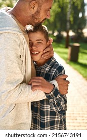 Caucasian father hug joyful teenage son with cerebral palsy look at camera in sunny park. Family relationship and spending time together. Disability care and rehabilitation. Fatherhood and parenting